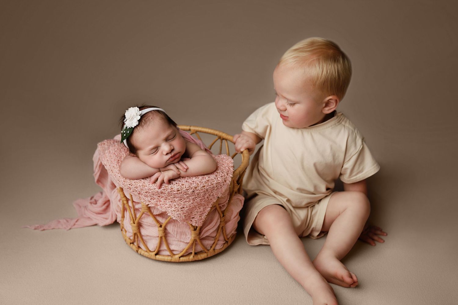 Sleeping newborn wrapped in beige swaddle lying in wooden heart-shaped bowl with knit blanket on brown background.