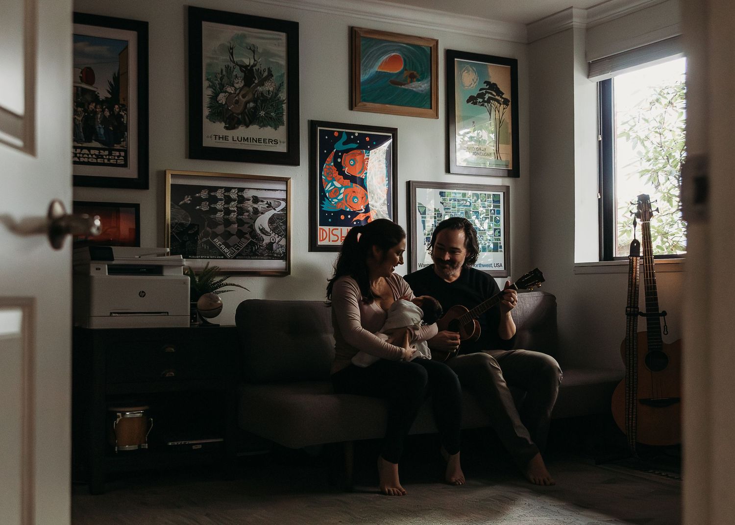 A panoramic view of a dimly lit room with framed artwork on walls and people sitting on furniture.