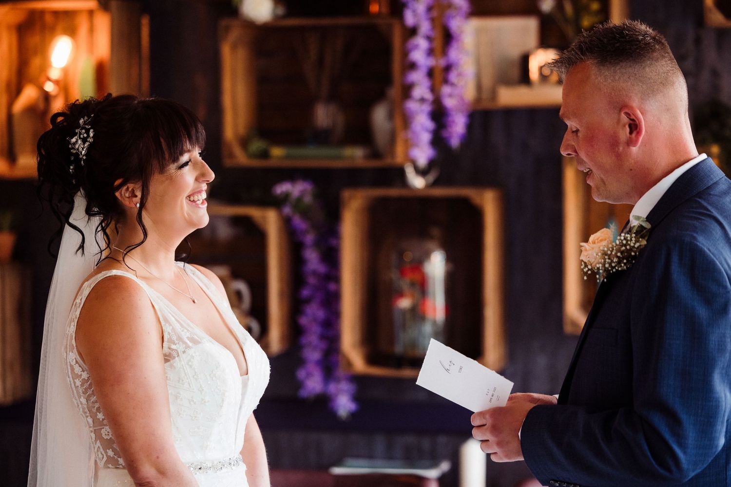 A couple shares an intimate moment during their wedding ceremony in a warmly lit venue with purple accents.