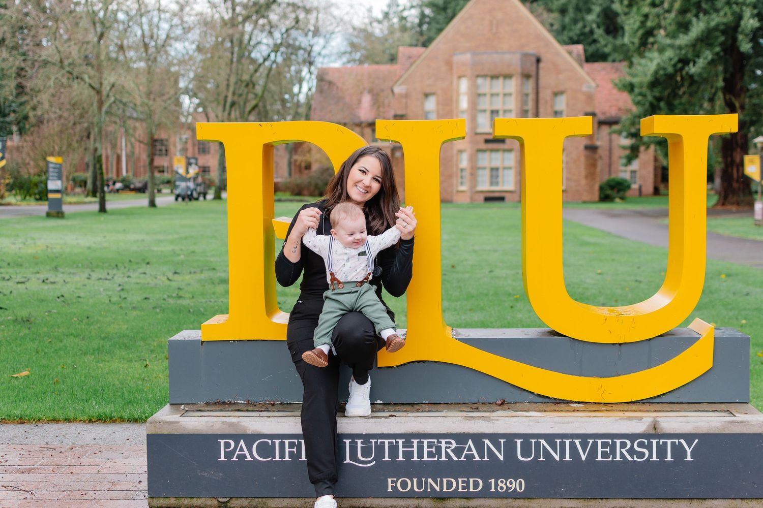 Graduation photos at the Pacific Lutheran University sign in Tacoma, Washington with nursing graduate and baby