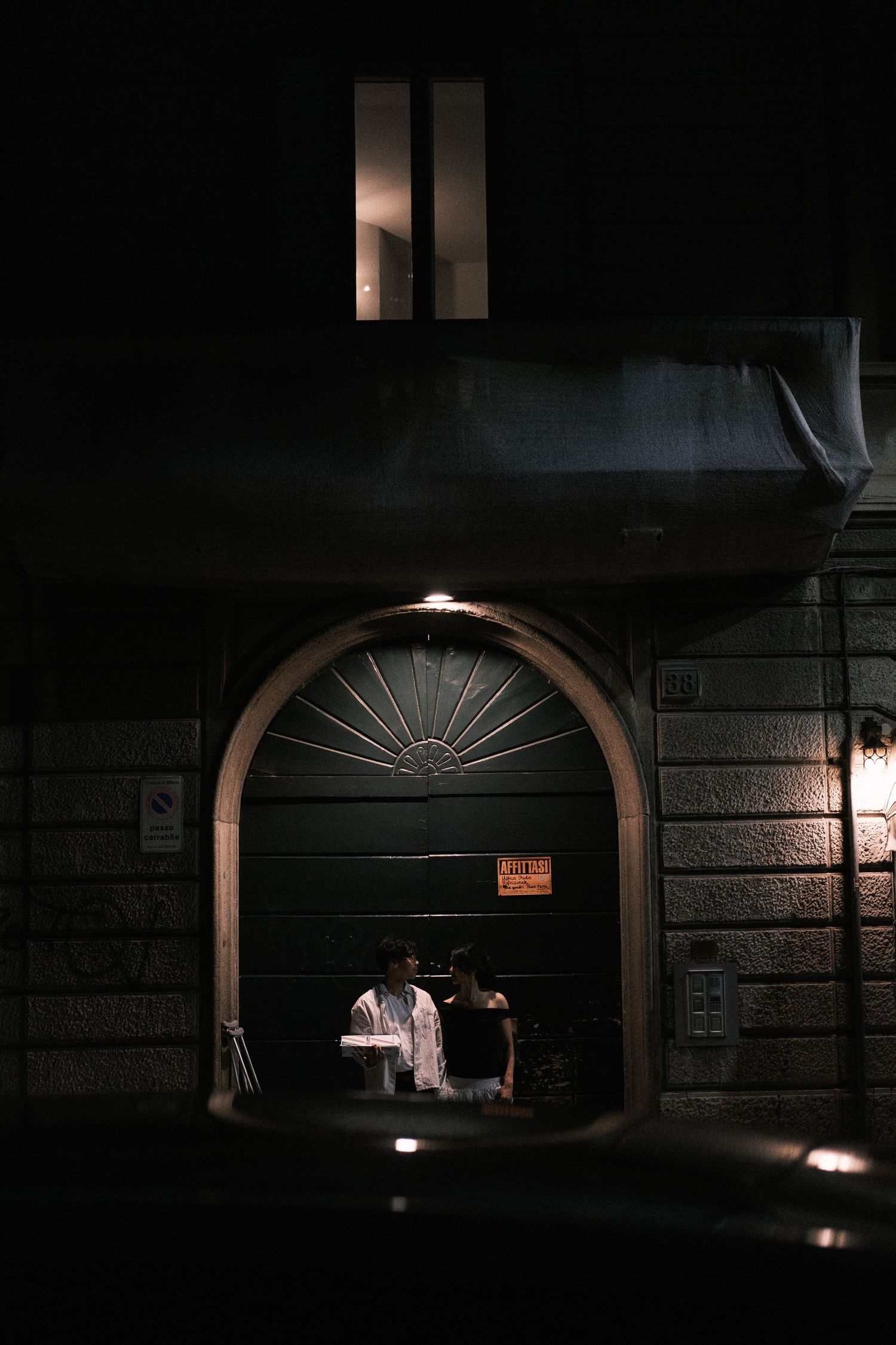 A dark architectural detail showing a series of illuminated arched doorways with decorative fanlight windows above.