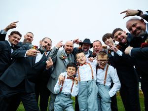 Wedding guests posing together outdoors on a grassy lawn for a fun group photo with animated expressions.