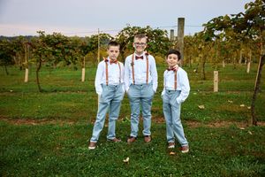 Groomsmen in light blue pants and suspenders pose together in a scenic apple orchard on a sunny day.