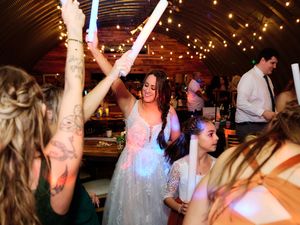 Wedding guests dance and celebrate on a dimly lit dance floor illuminated by warm string lights and colorful spotlights.