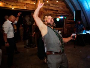 A group of party guests dancing and celebrating in a dimly lit rustic venue with wooden beams and ambient lighting.