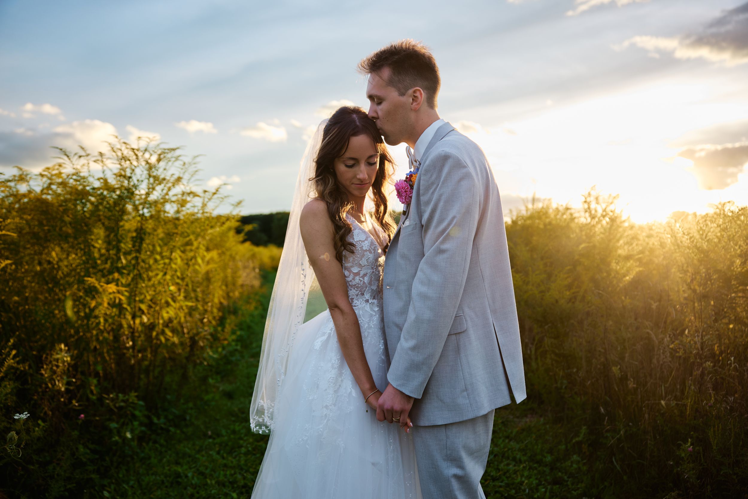 A couple embraces in a golden sunlit field of wildflowers during sunset creating a romantic silhouette.