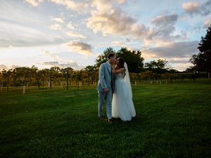 Couple walks hand in hand through a scenic vineyard at sunset with dramatic clouds in the sky.
