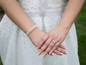 Close-up of hands wearing a pearl bracelet and diamond ring with a white beaded wedding dress in the background.