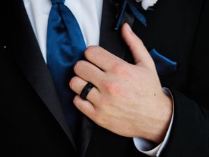 Close-up shot of hands adjusting a navy blue tie against a dark suit jacket.