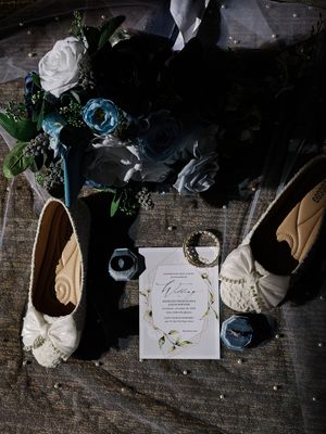 Wedding details flatlay with invitation, flowers, and accessories on rustic wooden surface.