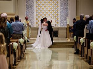 Wedding ceremony in a church with white patterned walls and guests seated in wooden pews.