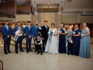 Wedding party members in blue and gray attire pose together in a formal church setting for group photos.