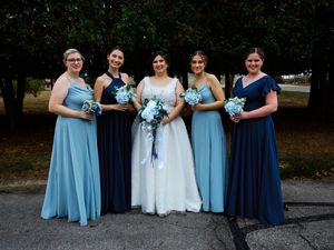 A bridal party poses outdoors wearing coordinated blue dresses in varying shades with light blue bouquets.