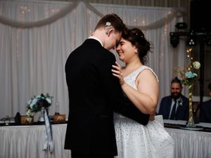 A couple shares an intimate dance moment at their wedding reception with white drapes and decor in the background.