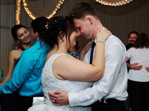 Couples dancing romantically under warm string lights at an indoor wedding reception.