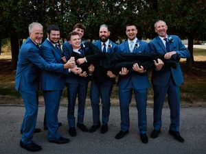 Groomsmen in matching blue suits pose playfully on the ground for wedding photos.