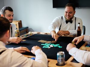 Friends gather around a black table playing a game with turquoise pieces while enjoying drinks and casual conversation.