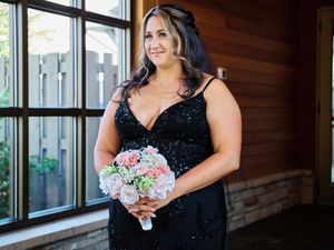 A group of bridesmaids in navy blue dresses hold bouquets while standing in a rustic wooden venue with windows.