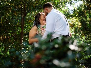 A romantic couple shares an intimate moment among lush greenery and trees during an outdoor photo session.