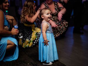 A small child in a light blue dress stands on a dance floor during a celebration.