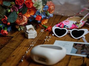 Heart-shaped sunglasses and colorful roses arranged on wooden surface with jewelry box and decorative elements.