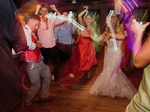 Wedding guests dance and celebrate on a dimly lit dance floor with colorful purple lighting in the background.