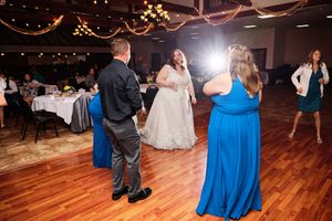 Wedding guests dance on a wooden floor during a reception with blue decor accents and ambient lighting.