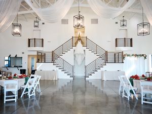 Elegant white wedding venue interior with grand staircases, hanging lanterns, and white dining tables.