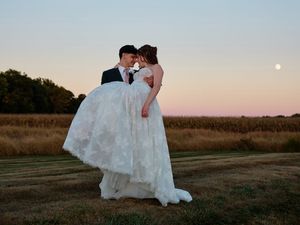 Wedding dress silhouettes against a sunset sky in an open field at golden hour.
