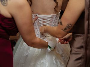 Someone helps adjust the corset lacing on an elegant white wedding dress with intricate details.