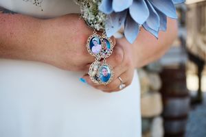 A delicate blue floral bouquet with a sentimental locket charm attached to the stems against a white dress.