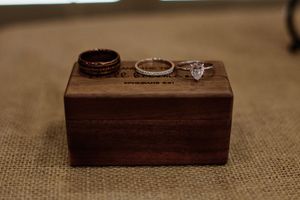 Two wedding rings and an engagement ring rest on a wooden box with burlap texture in warm lighting.