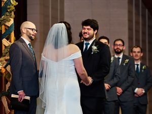 A wedding ceremony takes place at an elegant church altar with groomsmen standing in navy suits.