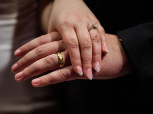 Two hands wearing wedding rings rest gently on top of each other, symbolizing marriage and commitment.