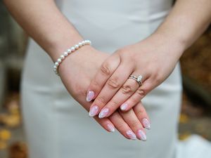 Close-up view of hands with pearl bracelet, engagement ring, and French manicured nails.
