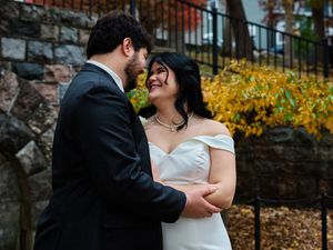 A couple embraces during an autumn wedding photoshoot with yellow foliage and stone walls in the background.
