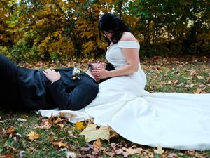 A couple in wedding attire rests on autumn leaves in a park during their romantic photoshoot.