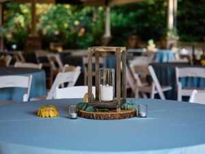 Wedding reception table centerpieces feature rustic wood slices with mason jars and candles on light blue tablecloths.