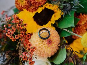 Vibrant autumn wedding bouquet with orange sunflowers, peach dahlias, and greenery arranged against a rustic background.
