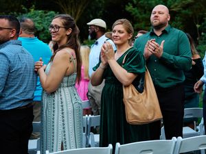 Wedding guests in formal attire react emotionally during an outdoor ceremony.