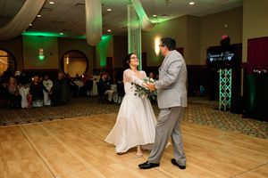 A couple shares their first dance as newlyweds on a wooden dance floor with green lighting in the reception venue.