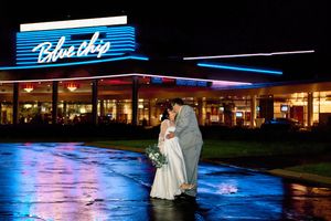 A couple shares a romantic moment in the rain outside a retro diner with blue neon lights.