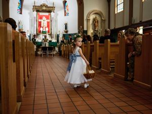 Wedding ceremony in a traditional church with wooden pews and religious statues along the aisle.
