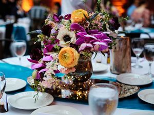 Elegant table settings with colorful floral centerpieces featuring orange roses and purple lilies at a reception.