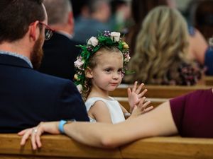 A child wearing a floral crown and white dress smiles during a wedding celebration.