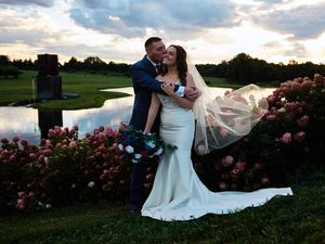 A romantic couple in wedding attire shares a tender moment at sunset in a garden filled with blooming roses.