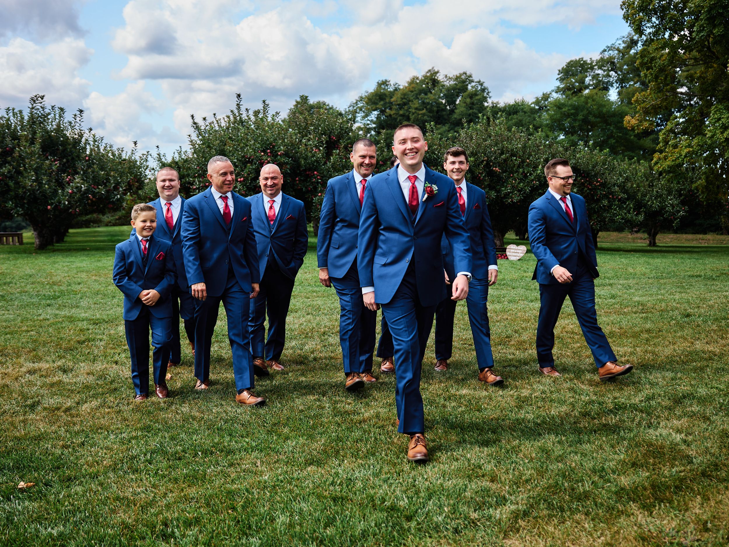 A group in matching blue suits poses playfully while laying in the grass during an outdoor photo session.