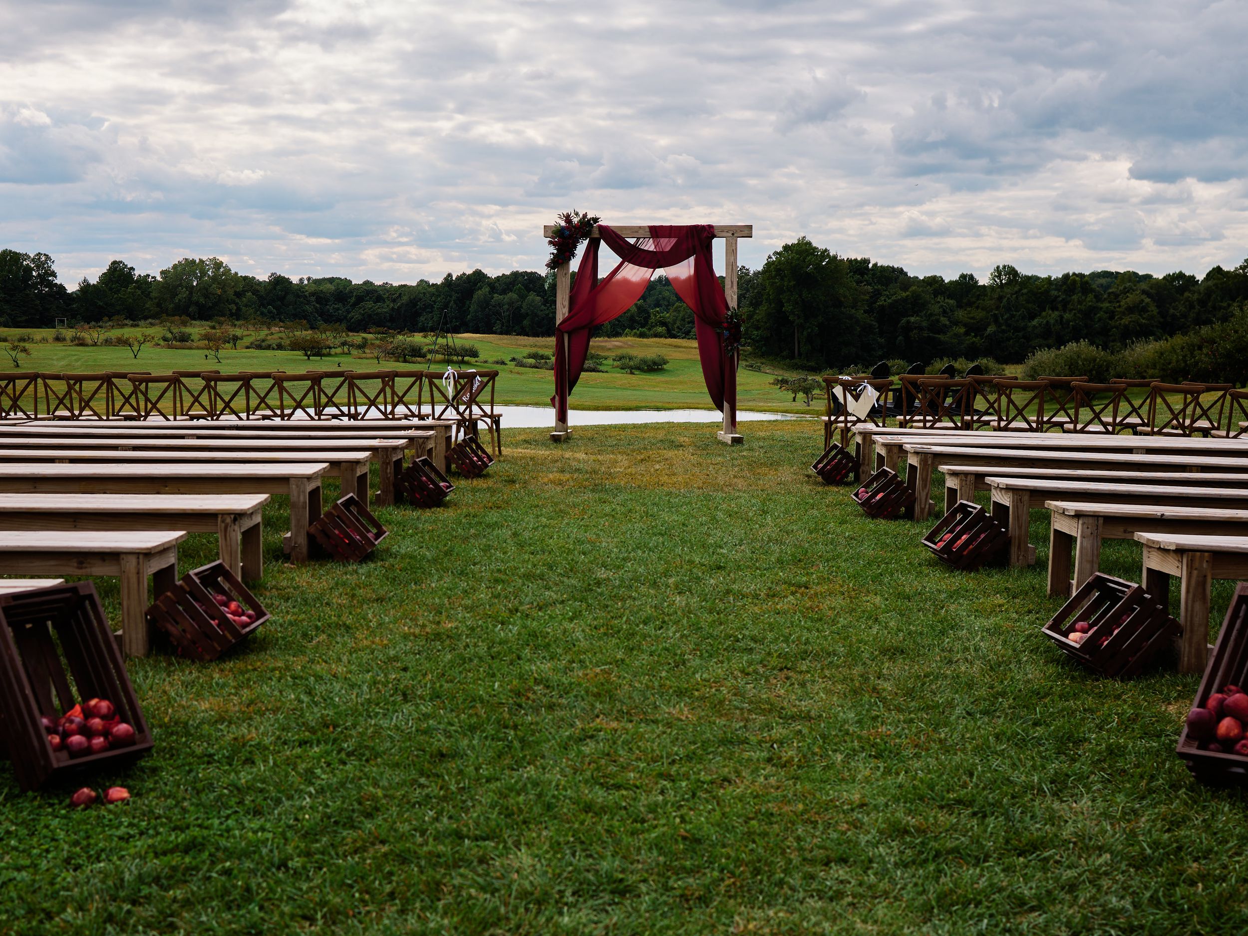 Rows of wooden benches arranged on a grassy lawn for an outdoor wedding ceremony with red floral decorations.