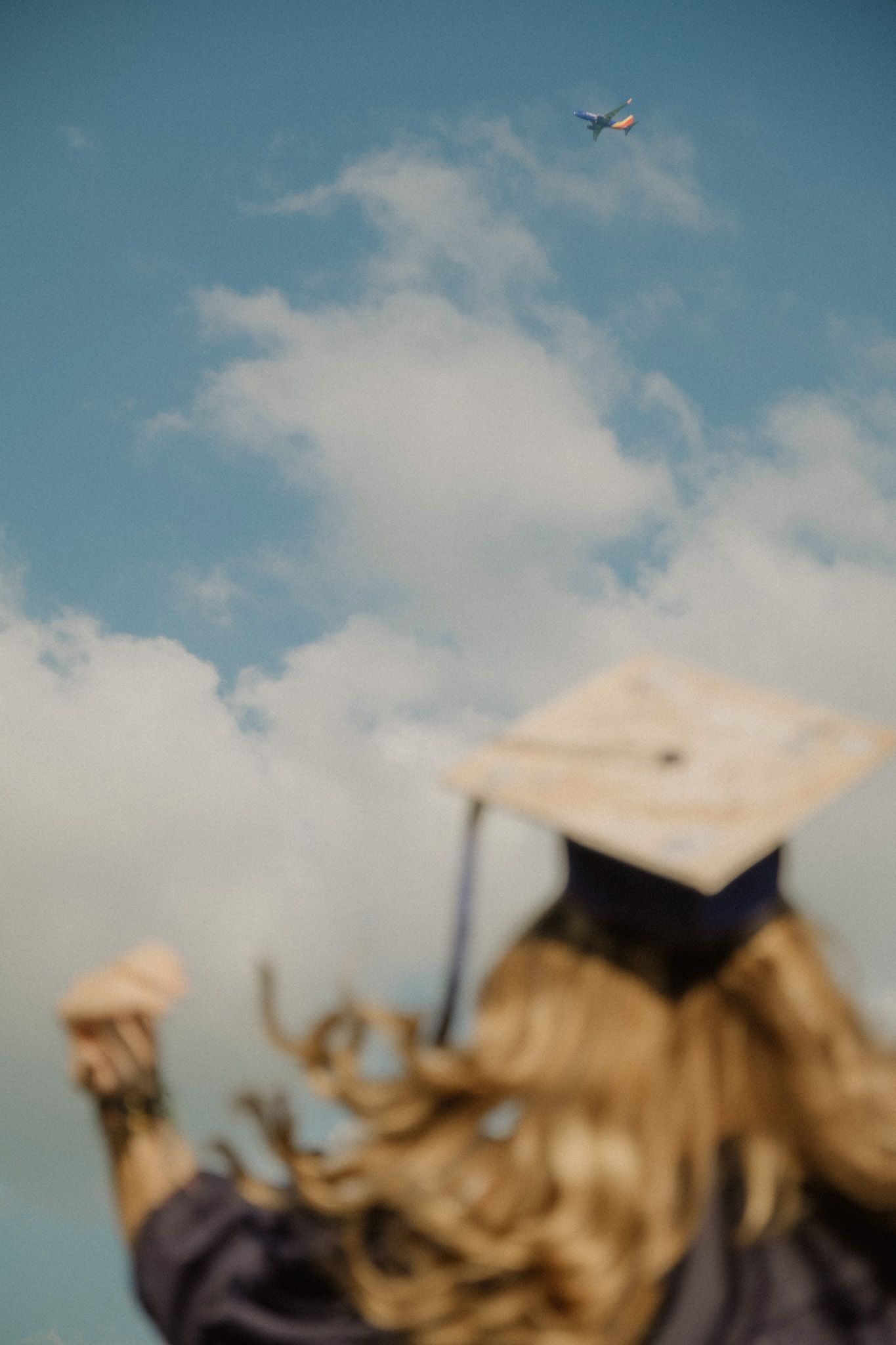 graduation photoshoot with girl against blue sky with airplane flying above.