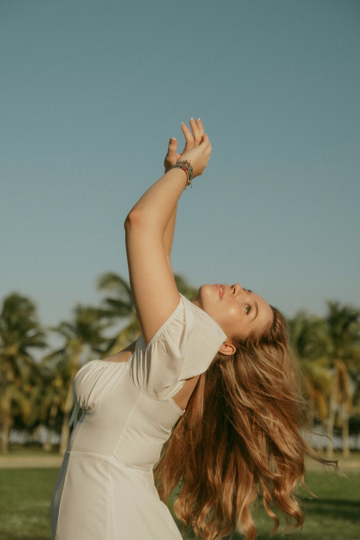 Figure in light clothing dancing joyfully outdoors with palm trees in background.